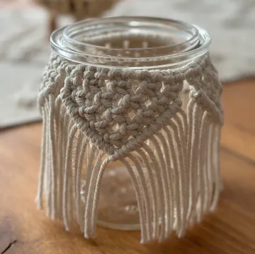 Glass container with decorative macrame closure on wooden table.