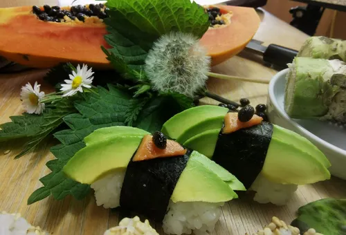 Sushi mit Avocado, umgeben von frischen Kräutern und Früchten.