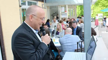 Mann spricht am Mikrofon vor einer Gruppe von Zuhörern.