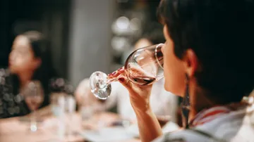 Eine Person trinkt Wein an einem Tisch mit Freunden.