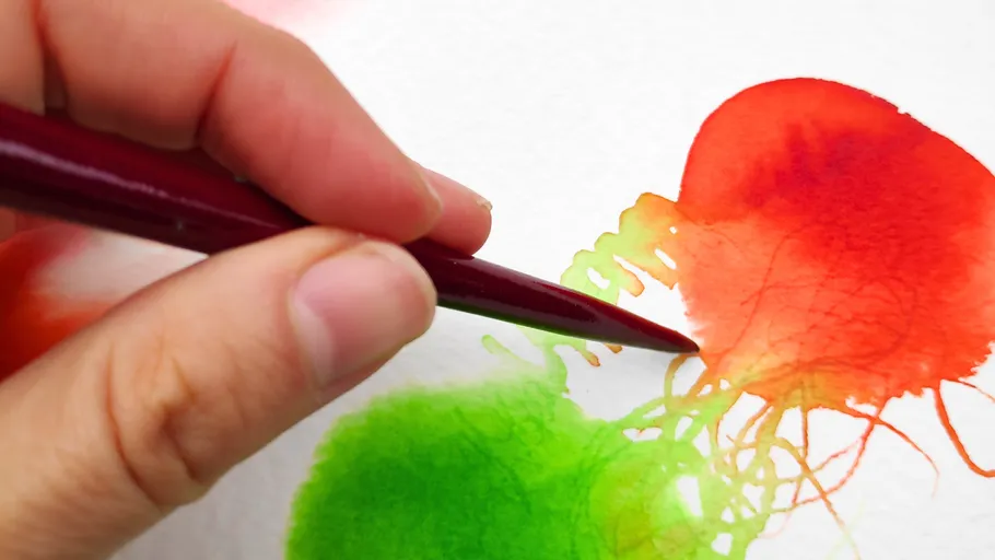 A hand paints on paper with a red pencil.