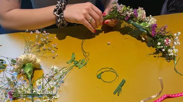 Hände binden Blumen zu einem Kranz auf einem Tisch.