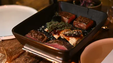 Black pan with grilled meat and herbs.