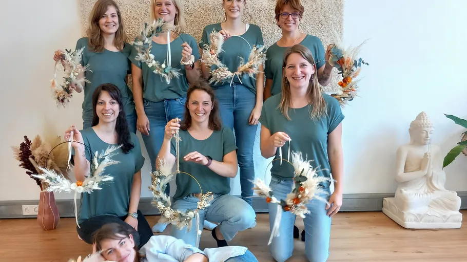 Ten women show autumnal floral wreaths in a room.