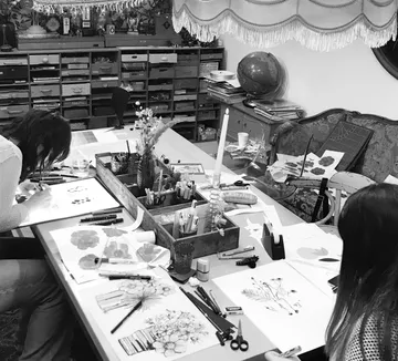 Table with female artists making flower drawings.