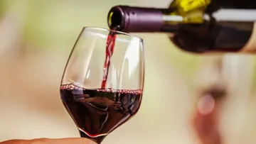 Rotwein wird in ein Glas gegossen, Hintergrund verschwommen.