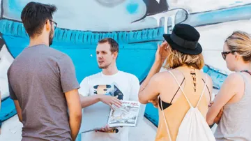 A group discusses in front of a colorful wall painting.