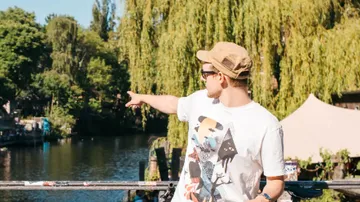 Young man points to a quiet river with trees.