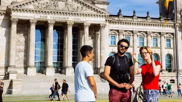 Three people stand in front of the Reichstag building and speak.