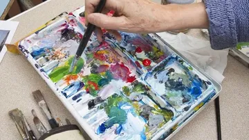 Pinsel mischt Farben auf einer Palette am Tisch.