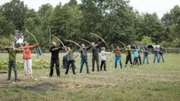 Gruppe Menschen zielt mit Bögen in einem Feld.