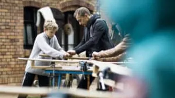 Zwei Personen arbeiten gemeinsam an einem Holzprojekt im Freien.