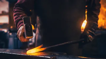 Blacksmith works glowing metal on anvil in workshop.