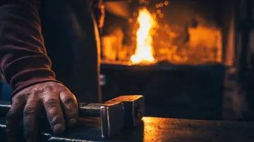 Hammer liegt auf Tisch, während Feuer im Hintergrund lodert.