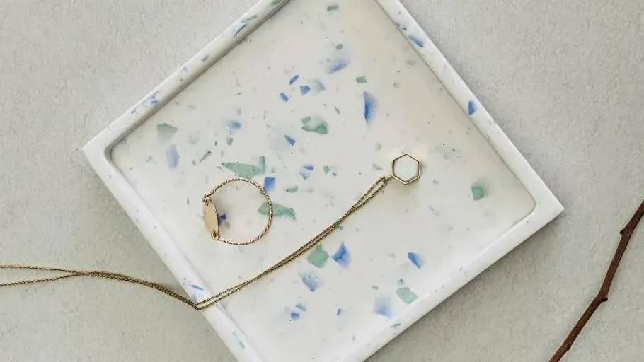 Golden pieces of jewelry lie on a bright, marbled tray.