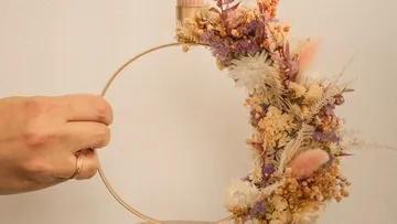 Hand hält dekorativen Kranz mit getrockneten Blumen.
