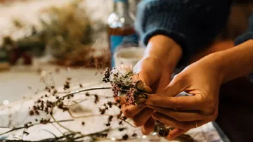 Hands arranging dried flowers on table.