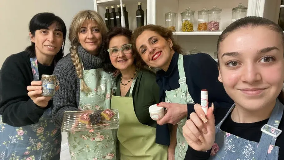 Fünf lächelnde Frauen, die Lebensmittel in der Küche in der Hand halten.