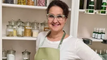 Frau mit Brille lächelt vor Regalen voller Zutaten.