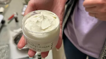 Eine Person hält eine Creme in einem Behälter.