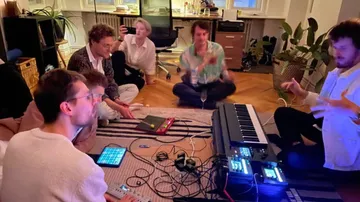 Musicians sit around electronic instruments and produce music creatively.