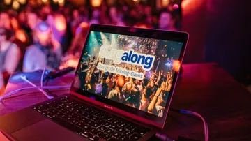 Laptop shows singalong event in a colorful, festive atmosphere.