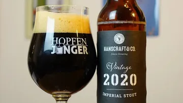A glass of beer stands next to a bottle.