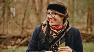 Frau lächelt, während sie eine Blätter im Wald hält.