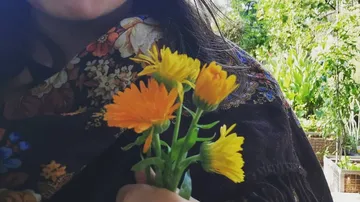 Person hält einen Strauß orangefarbener Blumen in der Hand.