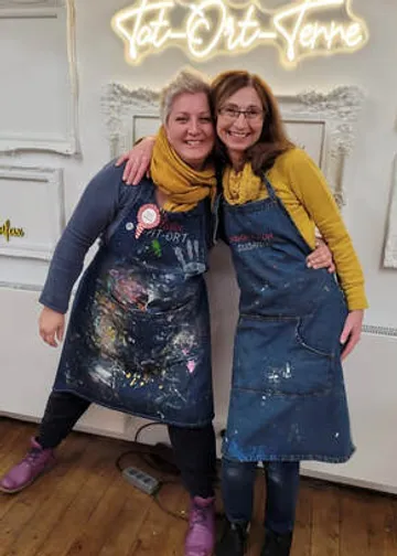 Two women smile together in painted aprons.