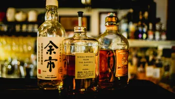 Three bottles of Japanese whiskey in a bar, elegantly arranged, with visible labels showcasing various brands.