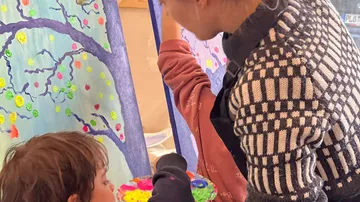 Kind beobachtet Malerin, die bunte Farben auf Leinwand anbringt.