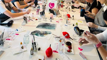 Artists work at a table with paint materials and tools.