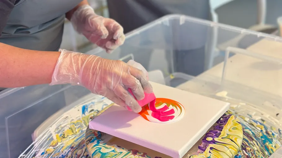A hand paints with pink paint on canvas in a creative space.