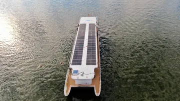 Solarboot schwimmt auf Wasser, umgeben von schwimmenden Menschen.