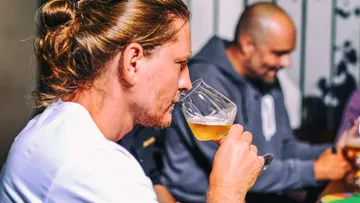 Mann trinkt Bier, umgeben von Freunden in einer Bar.