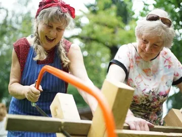 Zwei Frauen schneiden Holz im Freien, sichtbar freundlich.