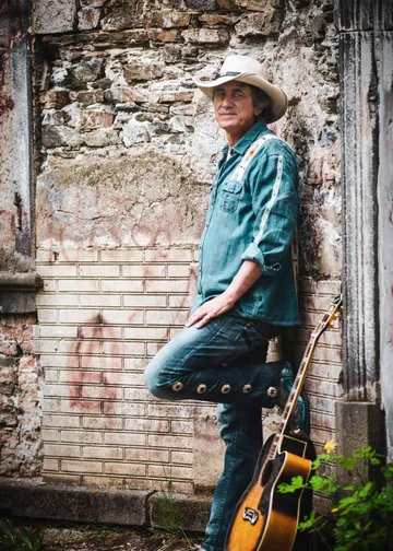 Mann lehnt an einer Mauer mit einer Gitarre daneben.