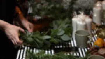 Hands form a wreath of green branches on the table.