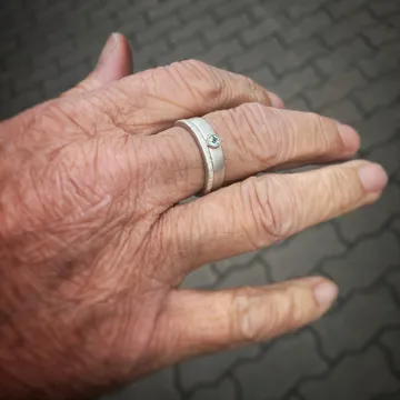 Hand mit Ringen zeigt gestochenes Zeichen auf Pflastersteinen.