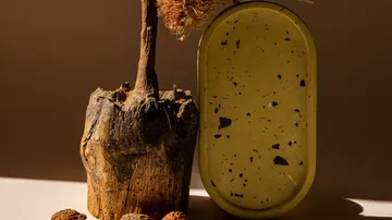 Wooden boat with dried flowers next to yellow bowl on table.