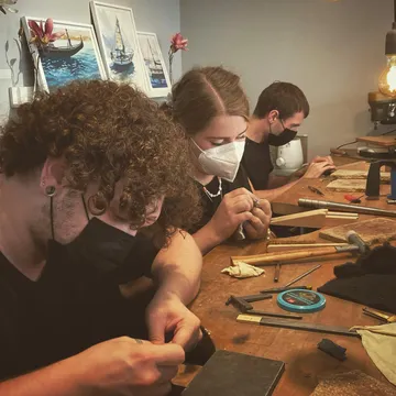 Three people work on jewelry in a studio.