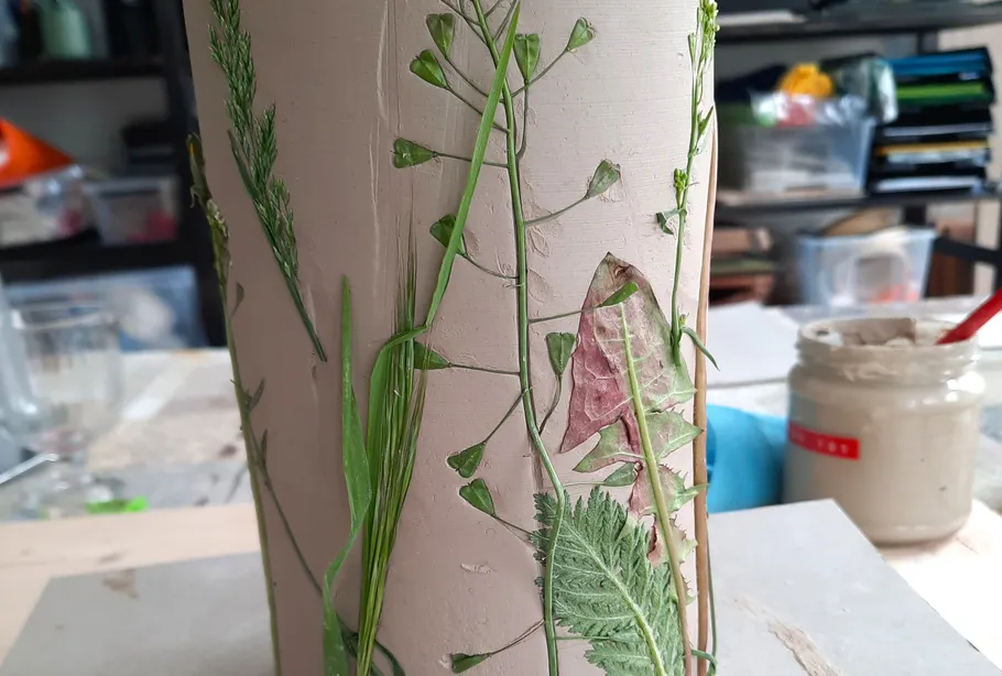 Ein zylindrisches Objekt ist mit Pflanzenblättern dekoriert.