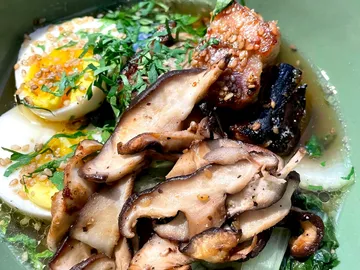 Bowl with mushrooms, eggs and fresh herbs in broth.
