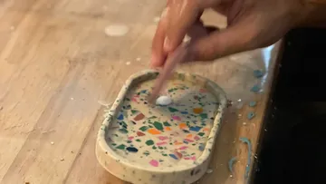 Hand stir in colorful, liquid material in bowl.