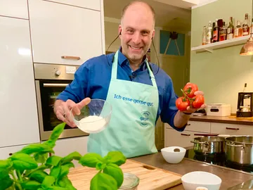 Kocher hält Tomaten und Mehl in moderner Küche.
