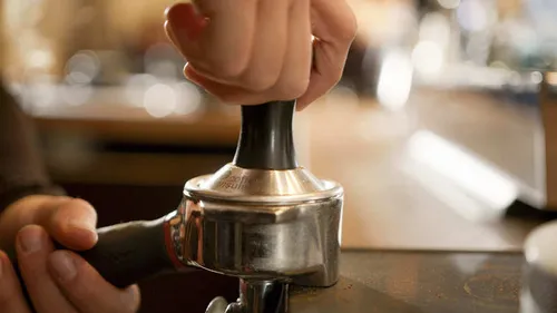 Eine Hand drückt auf einen Kaffeepresso-Tamper auf einer Oberfläche.