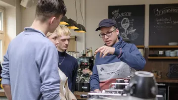 Three people learn how to make coffee in a café.