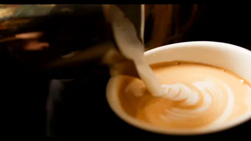 Milch wird in eine Kaffeetasse gegossen; gemütliche Atmosphäre.