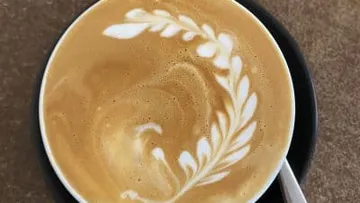 Kaffeetasse mit kunstvollem Milchschaummuster auf Holzuntergrund.